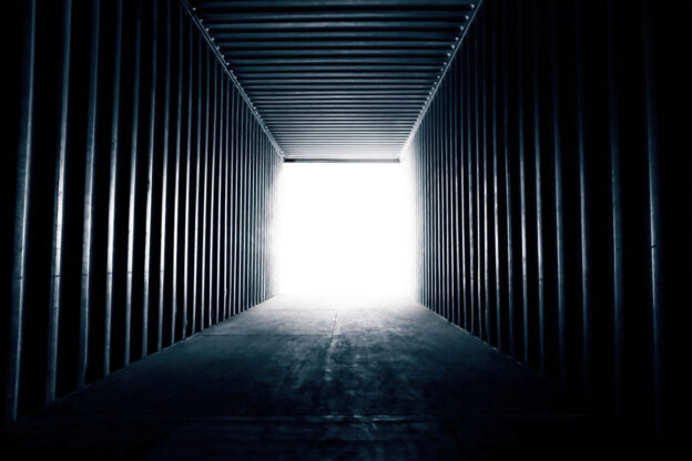 The inside of a shipping container looking outward; light is shining in from the opening.